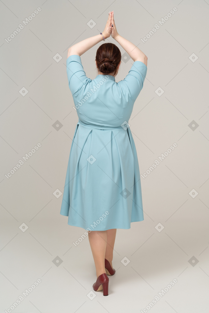 頭の上に手をポーズでポーズをとって青いドレスを着た女性の背面図