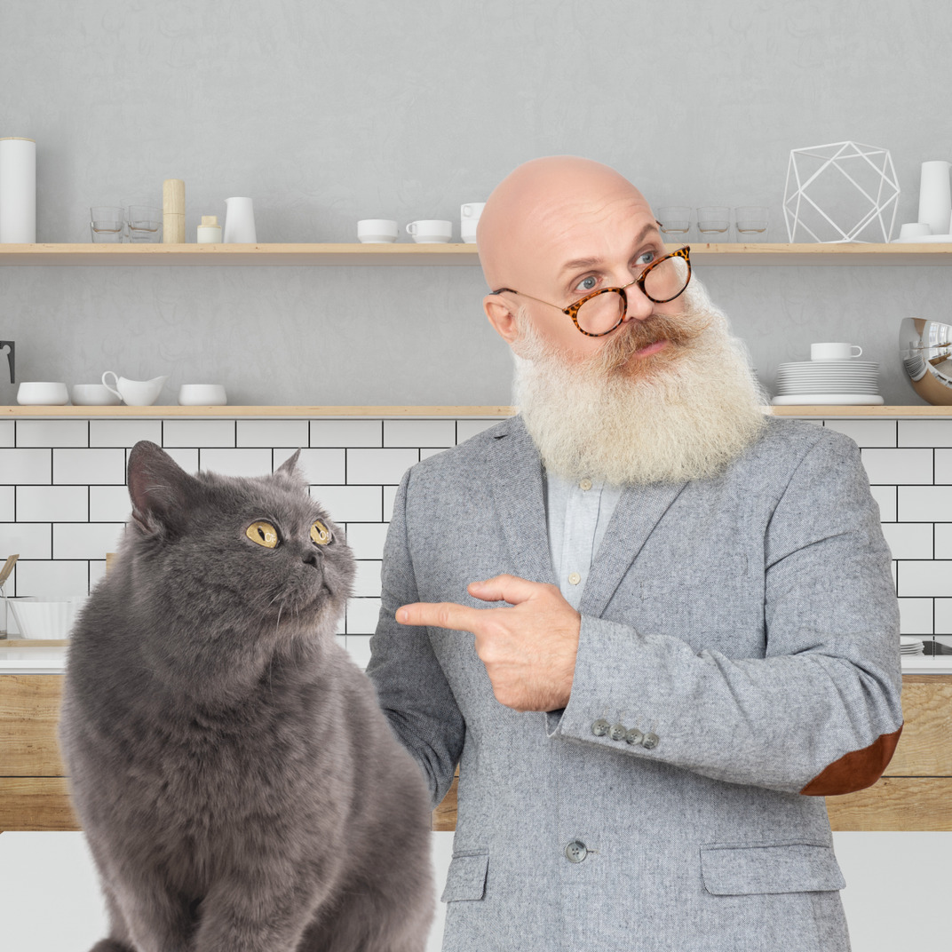 Older man standing in kitchen and pointing on cat