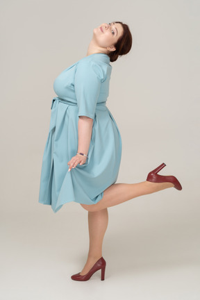 一个穿着蓝色连衣裙、单腿摆姿势的女人的侧视图
