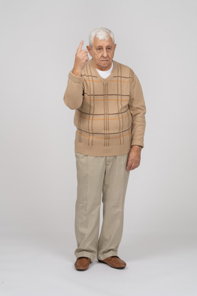 Front view of an old man in casual clothes pointing up with finger