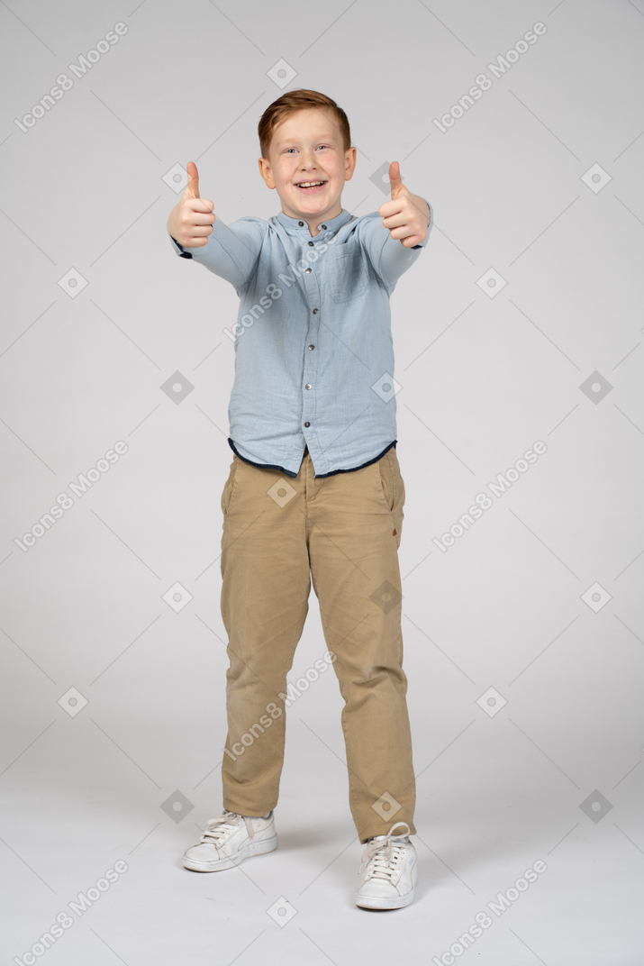 親指を立ててカメラを見ている幸せな少年の正面図
