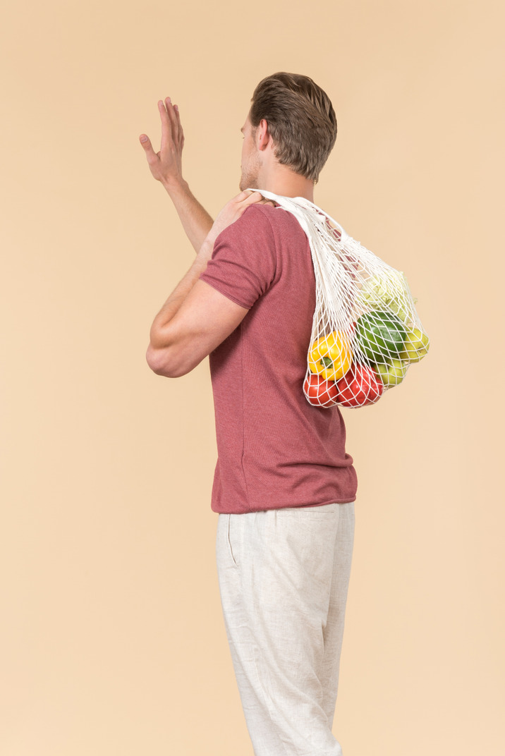 Young guy holding a string bag with groceries and waving