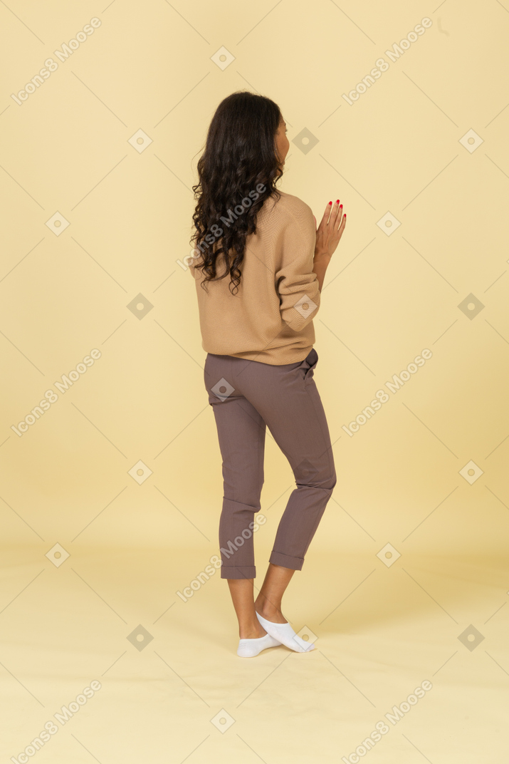 Three-quarter back view of a dark-skinned young female raising her hands