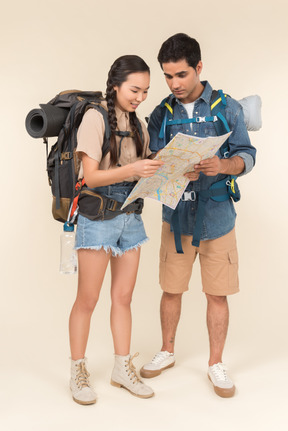 Jovem homem e mulher com mochila enorme olhando atentamente no mapa