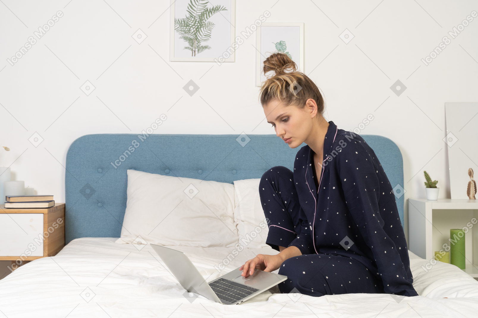 Side view of a young female sitting in bed with her laptop
