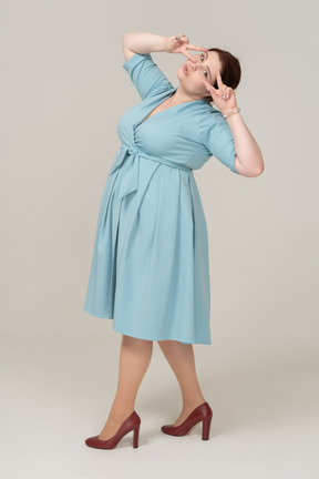 Side view of a woman in blue dress showing v sign