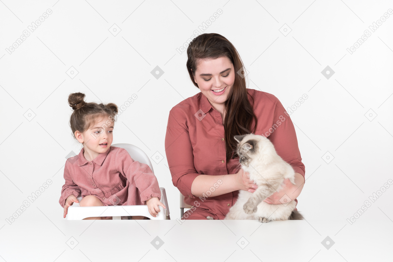 母亲和她的小女儿，穿着红色和粉红色的衣服，坐在餐桌旁与他们的家猫