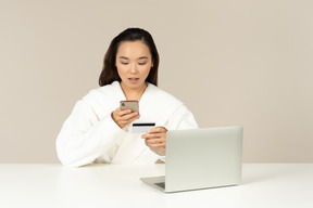 Молодая азиатская женщина используя телефон и проверяя карточку