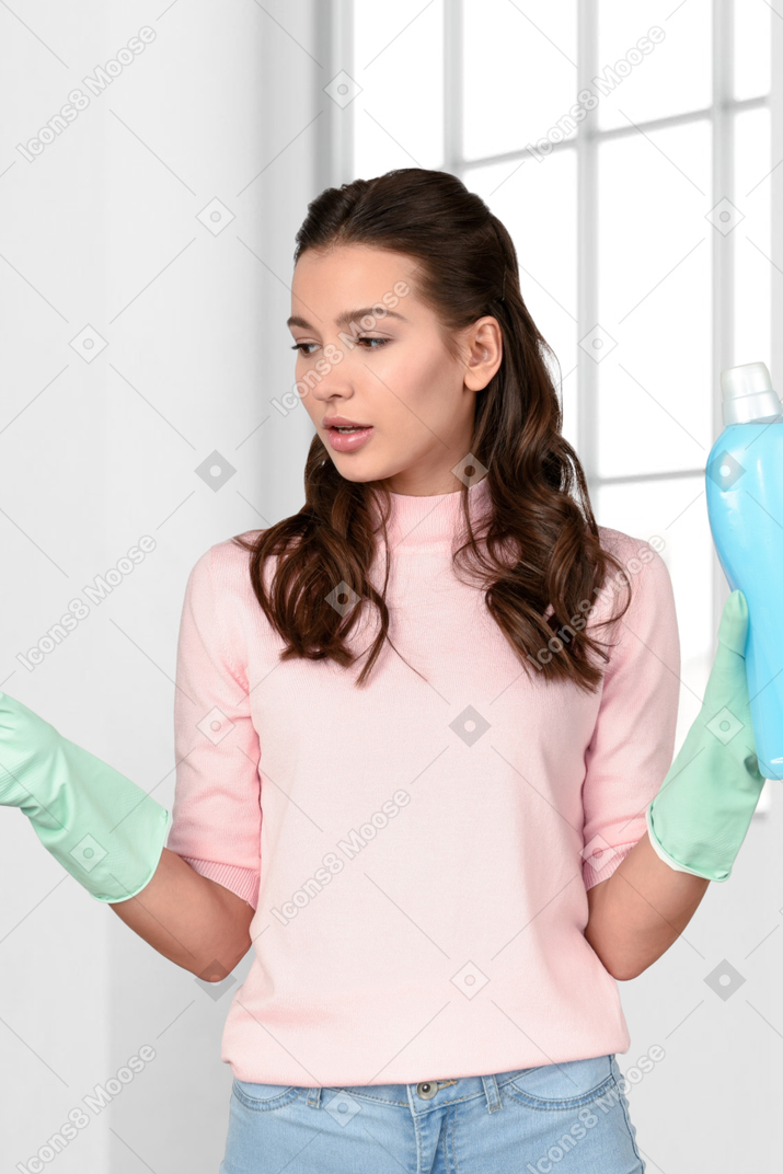A woman in a pink shirt and green gloves holding a blue bottle