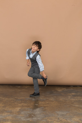 一个穿着灰色西装的可爱男孩站在一条腿上的正面图