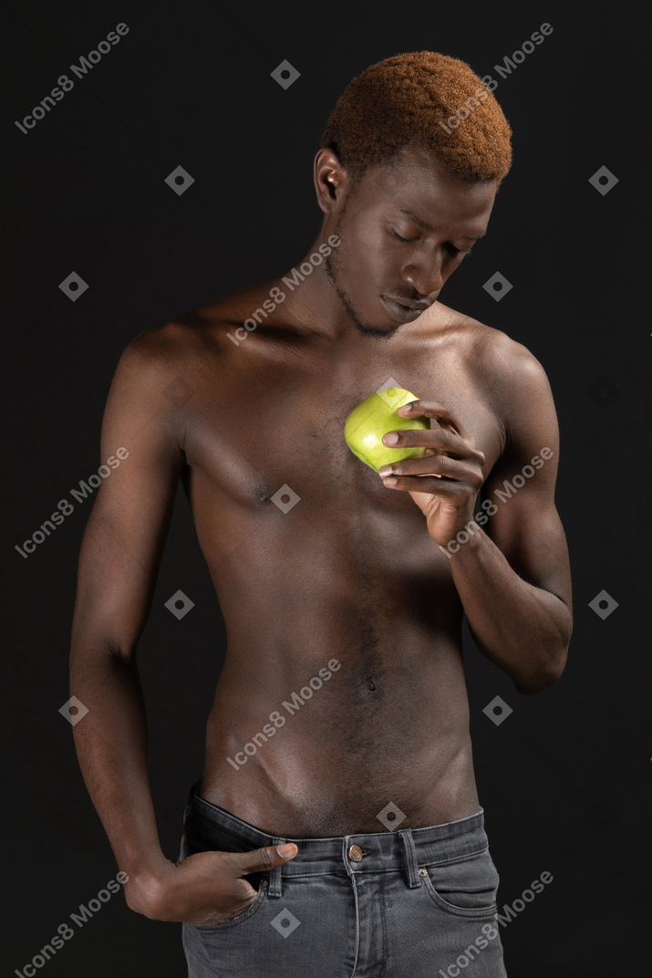 Крупным планом африканец внимательно смотрит на свое зеленое яблоко