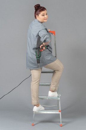 Woman standing half-way round on stepladder with a drill