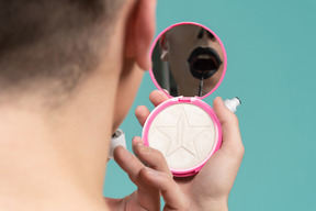 Back view of a person holding mirror and putting on lipstick