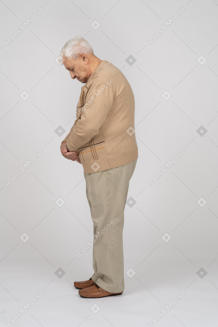 一位穿着休闲服的老人站着不动，向下看的侧视图