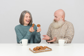 Donna invecchiata ridendo forte mentre tiene i biscotti e suo marito non capisce