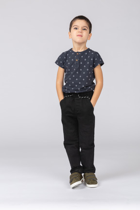 Вид спереди симпатичного мальчика, стоящего с руками в карманах и смотрящего в камеру