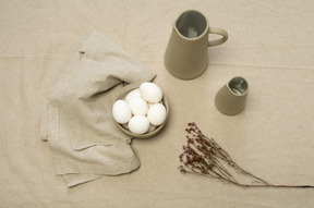 A bowl of chicken eggs and some jars on a grey tablecloth