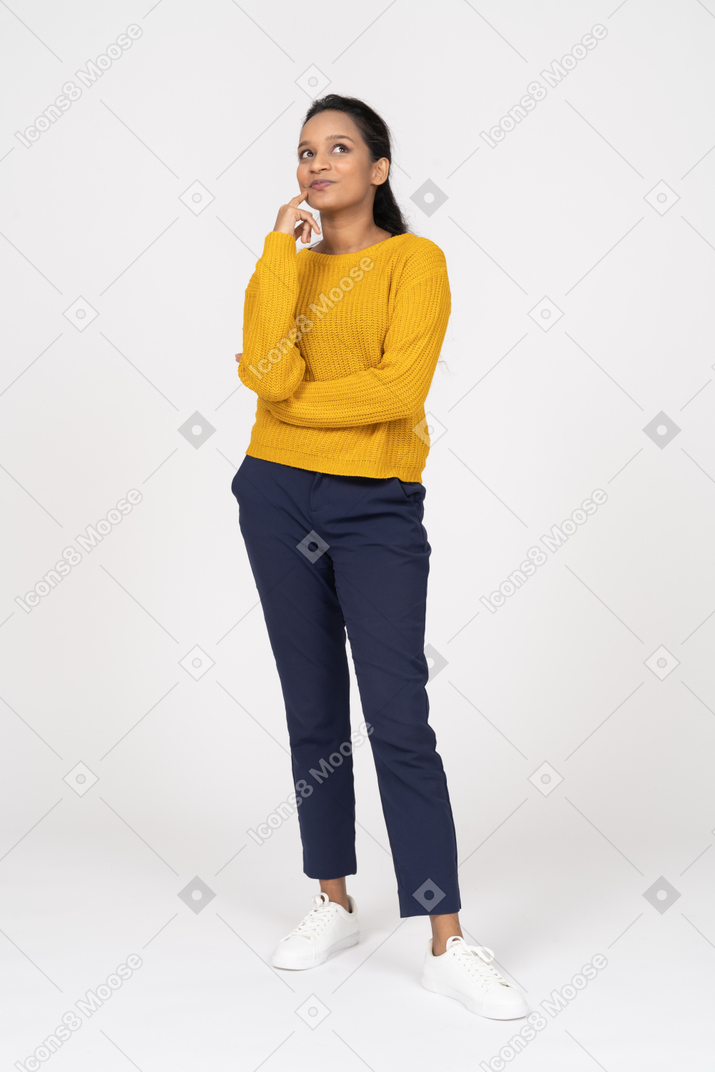 Вид спереди задумчивой девушки в повседневной одежде, смотрящей вверх и касающейся пальцем подбородка