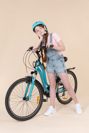 Dreamy teenage girl in blue helmet riding on bicycle