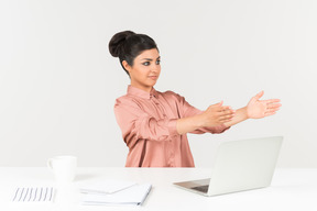Молодая индийская женщина сидит на офисном столе и указывая обеими руками