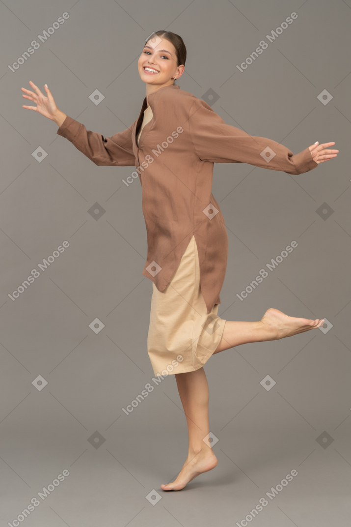 Mulher sorridente em pé descalço com a perna esquerda levantada no ar