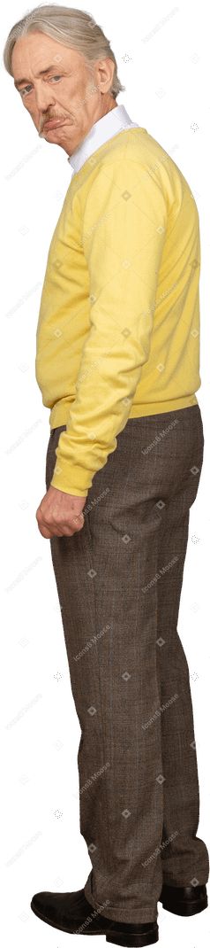 Vue latérale d'un vieil homme mécontent dans un pull jaune regardant la caméra