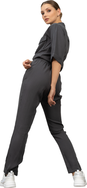 Three-quarter back view of a young woman in a jumpsuit making a step