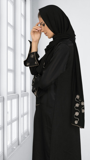 A woman in a black hijab standing by a window