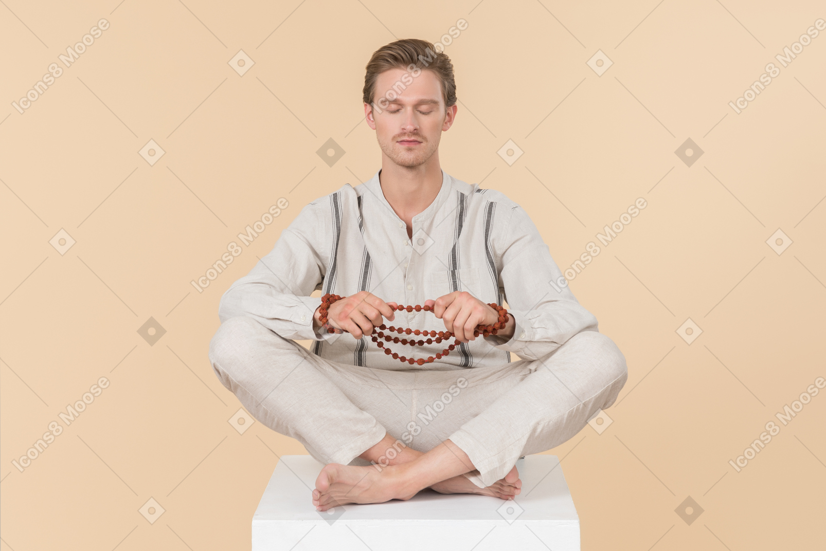 Young caucasian man sitting in lotus position holding necklace