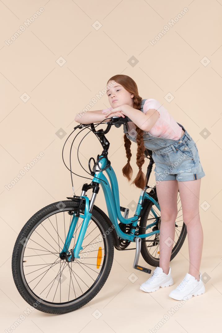Bored looking teenage girl leaning on bicycle