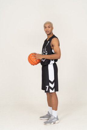 Vista lateral de un joven jugador de baloncesto masculino sosteniendo una pelota