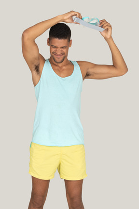 Man in blue tank top and yellow shorts taking off swim mask