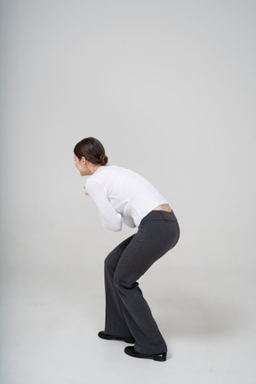 Side view of a woman in black pants and white blouse bending down