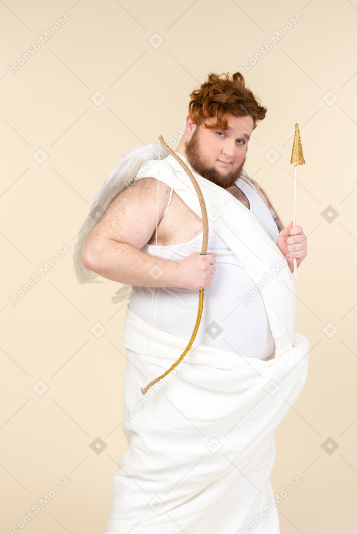 Cunning looking young big man dressed as a cupid holding bow and arrow