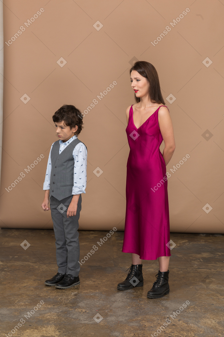 男の子が彼女の近くに立っている間、背中の後ろに腕を持っている赤いドレスの女性