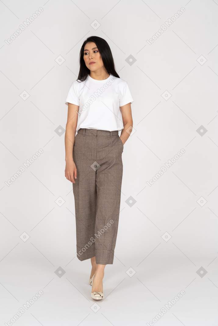 Front view of a walking bored young lady in breeches and t-shirt putting hand in pocket