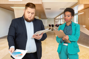 A man with papers standing next to a woman with clipboard