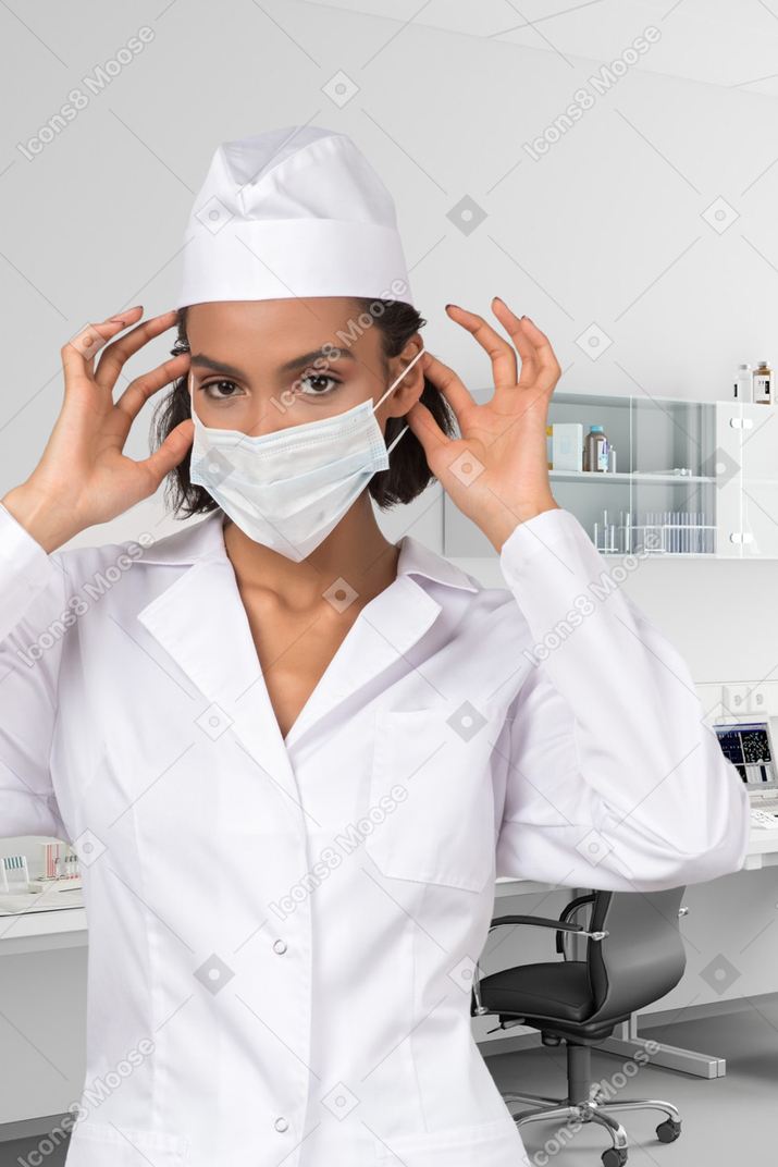 A woman wearing a white lab coat and a surgical mask
