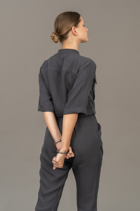 Three-quarter back view of a young woman in a jumpsuit wearing handcuffs