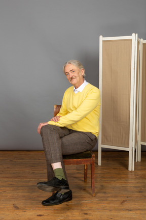 Uomo sorridente seduto a gambe incrociate sulla sedia