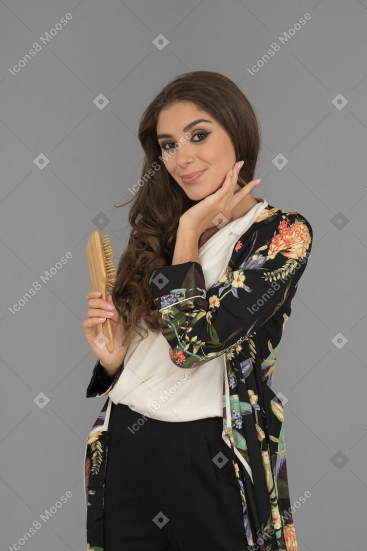 Attractive brunette female holding hairbrush and facing camera