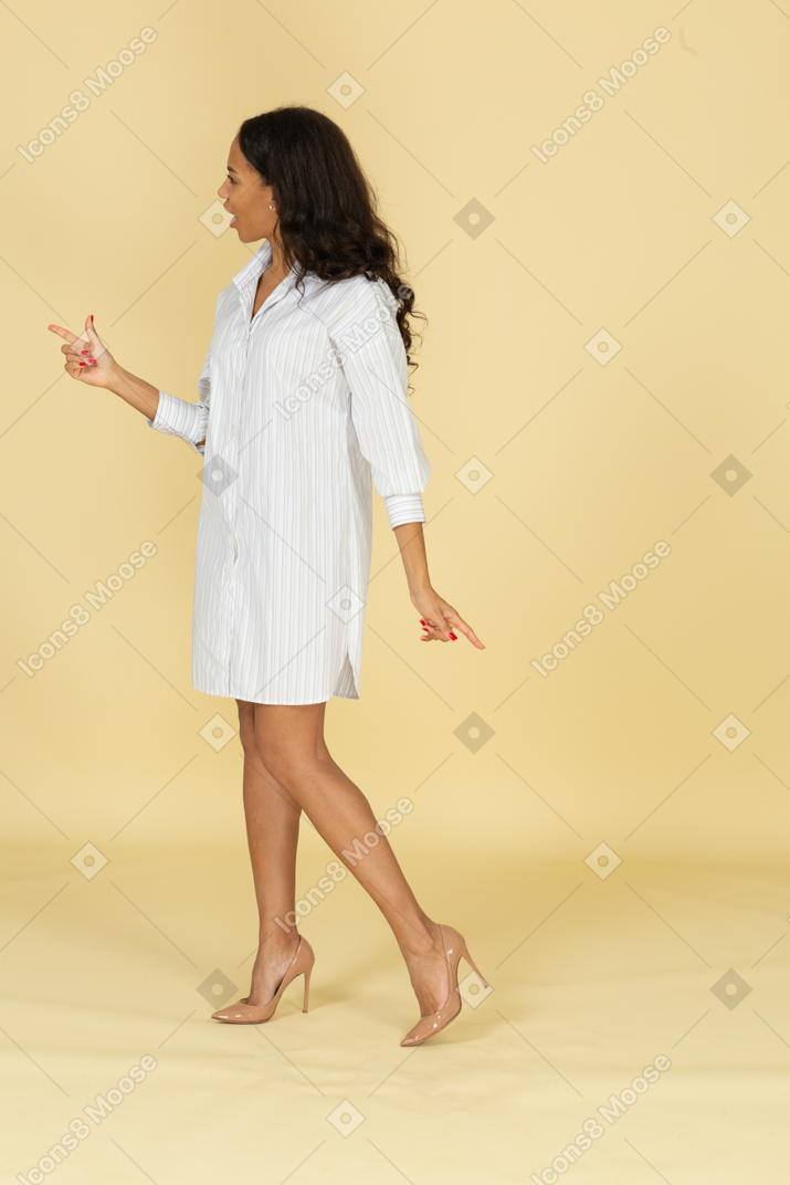 Vista de tres cuartos de una mujer joven de piel oscura cuestionando en vestido blanco levantando la mano