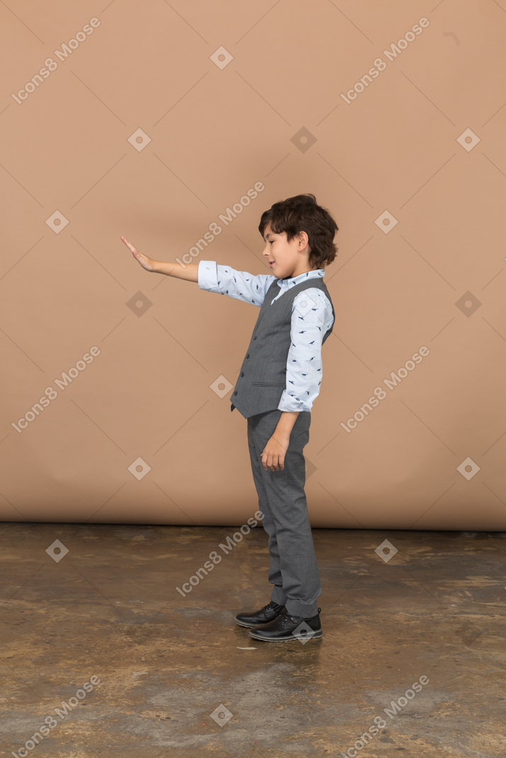 Side view of a boy in grey suit standing with outstretched arm
