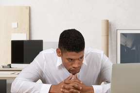 Puzzled man sitting at a desk looking at a laptop