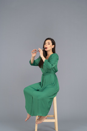 Full-length of a young lady in green dress sitting on a chair while playing the clarinet