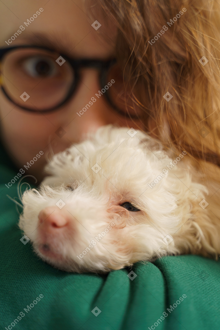Young female wearing glasses and cuddling with her little poodle and looking at camera