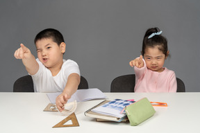 Boy and girl pointing forward while sitting at desk