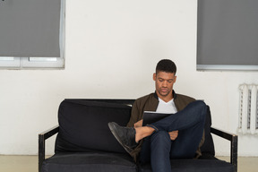 Front view of a young man sitting on a sofa while holding tablet