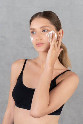 Young woman wiping cream off her face with cotton pad