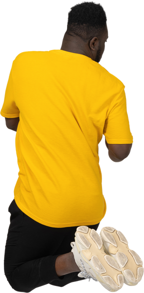 Vista traseira de um jovem de pele escura pulando em uma camiseta amarela
